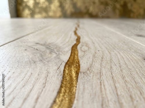White oak wood floor with filled crack using gold resin. Kintsugi interior design technique for modern home renovation. Luxury texture pattern with metallic inlay and wood grain.