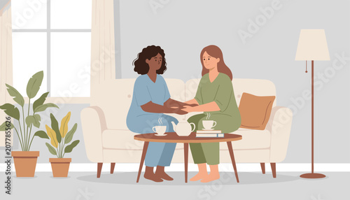 Two female friends sitting on a sofa, holding hands, and sharing a comforting moment with hot tea in a living room.