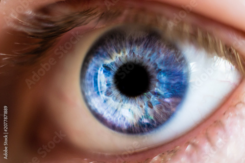 An extreme close-up macro photograph capturing the intricate textures and vibrant, varied blue hues of a human iris surrounding a dilated pupil.
