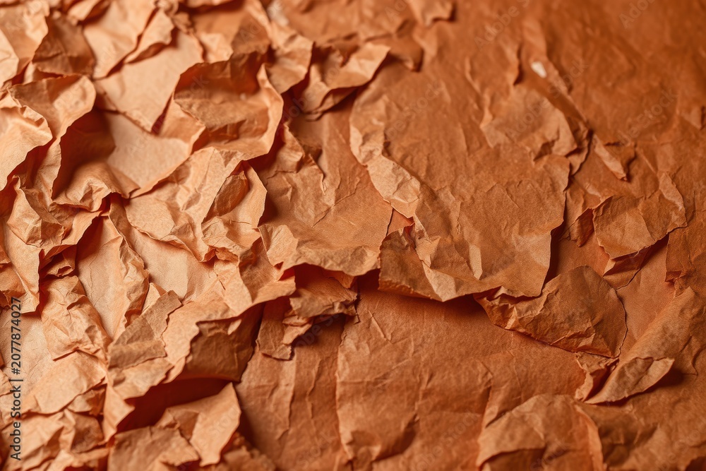 Fototapeta premium Crumpled paper texture fills frame. Warm brown tones dominate, creating abstract background. Wrinkles suggest fragility, decay.