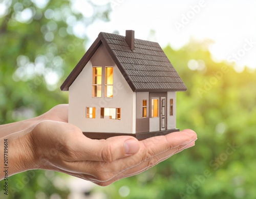 Hands holding a miniature model of a house against a blurred background