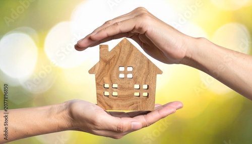 Hands holding a miniature model of a house against a blurred background
