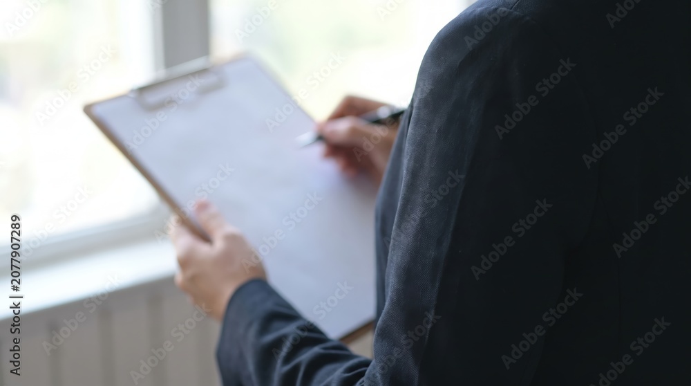 Obraz premium Over the Shoulder Close-Up of Businesswoman in Corporate Attire Writing on Clean Minimalist Checklist with Pen, Focusing on Project Management, Task Organization, and Productivity Growth Concept