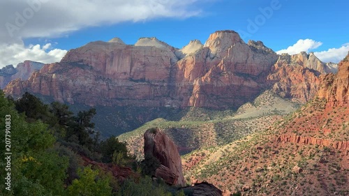 Zion National Park canyon cliffs in Utah, red sandstone mountains rise above a green valley under dramatic clouds and bright blue sky
