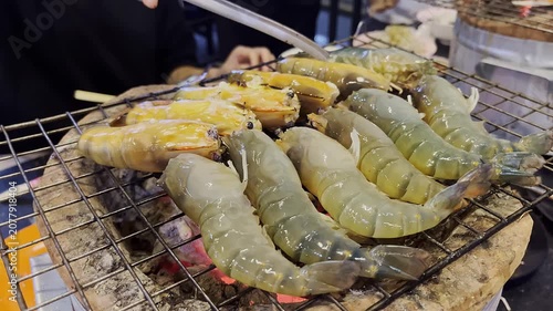 Delicious fresh shrimp barbecue on charcoal grill mesh at street food market. Close up of giant river prawn grilling on traditional charcoal stove.
