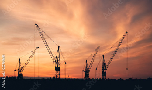 Construction cranes silhouette at sunset sky, industrial landscape with copy space