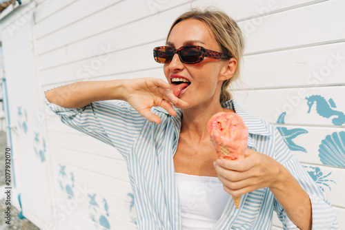 Woman enjoying a melting strawberry ice cream cone on a sunny summer day by the seaside