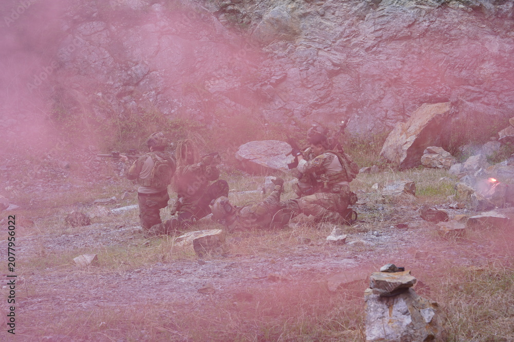 Fototapeta premium multinational group of male soldiers in infantry uniforms, carrying paintball guns and ready for combat, were seen running and practicing military drills, with pink smoke signals being sent 