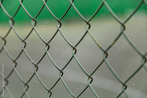 Bild auf Leinwand Close-up of a metal chain-link fence in perspective against a blurred green sports field background