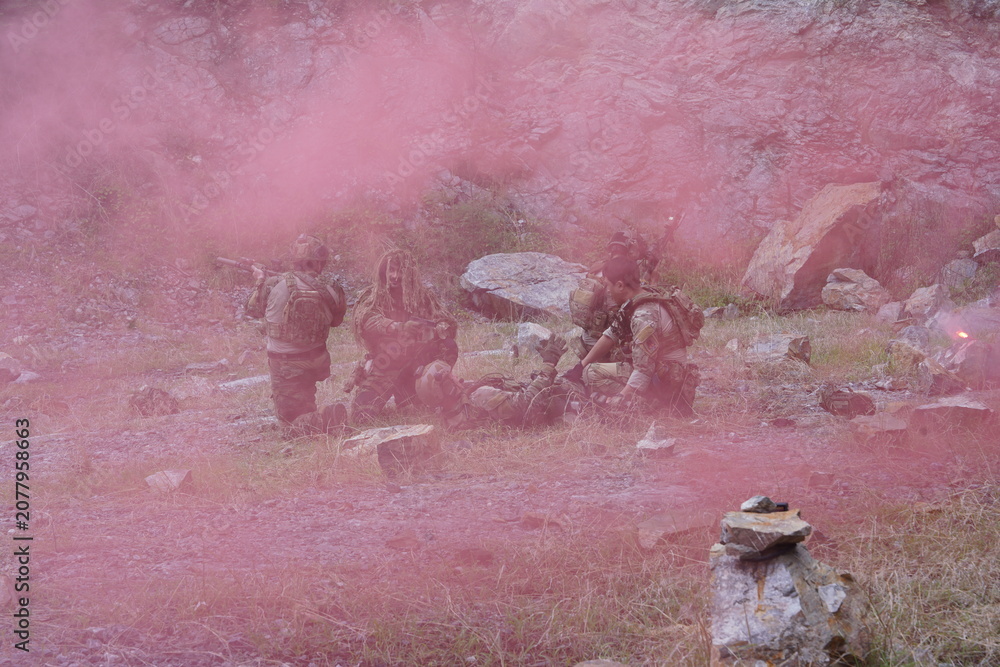Fototapeta premium multinational group of male soldiers in infantry uniforms, carrying paintball guns and ready for combat, were seen running and practicing military drills, with pink smoke signals being sent 