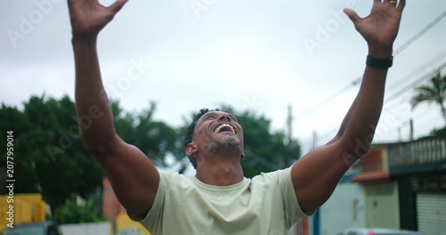 Schilderij op canvas Man of African descent standing on urban street with arms raised, looking up in