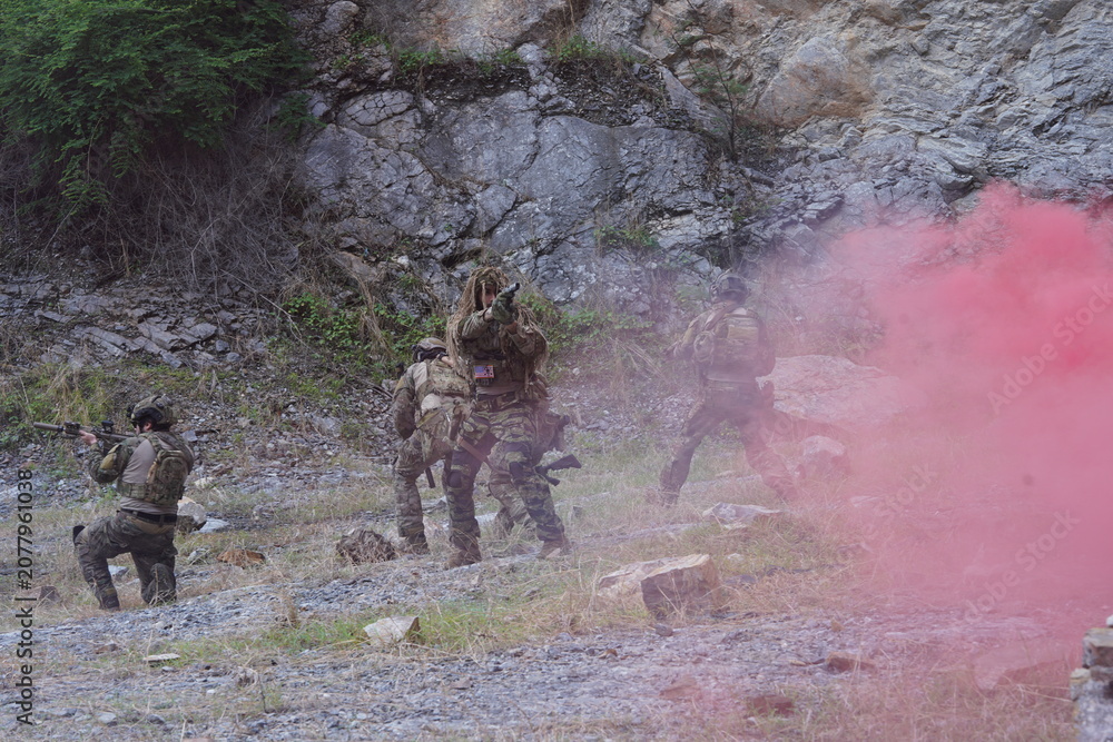 Fototapeta premium multinational group of male soldiers in infantry uniforms, carrying paintball guns and ready for combat, with pink smoke grenades and practicing military drills, with pink smoke signals