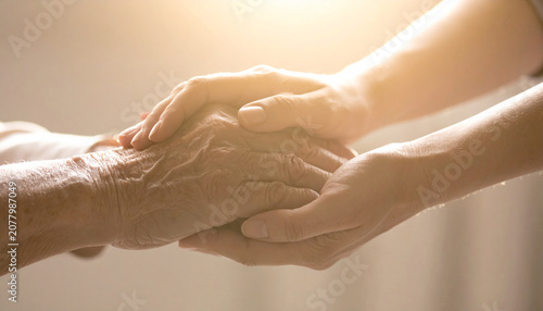 A Gentle Touch: A pair of hands, one aged and wrinkled, the other younger and smoother, clasped together in a gesture of comfort, compassion, and support, bathed in soft, warm light.