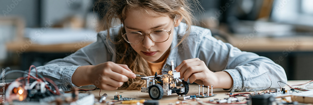 Naklejka premium Young girl focused on building a robot with electronic components at a workshop.
