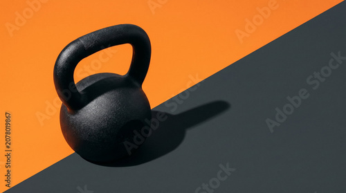 Heavy iron kettlebell in minimalist split style, black, orange, and dark grey tones, strength training or fitness workout mockup with copy space