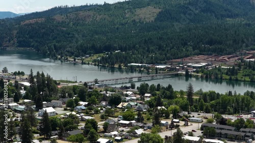 Aerial of small town on the Priest River with bridge and forest in Priest River Idaho in summer time with mountain backdrop