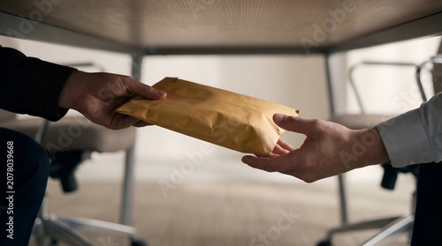 Business people secretly passing an envelope under the table in corporate bribery concept