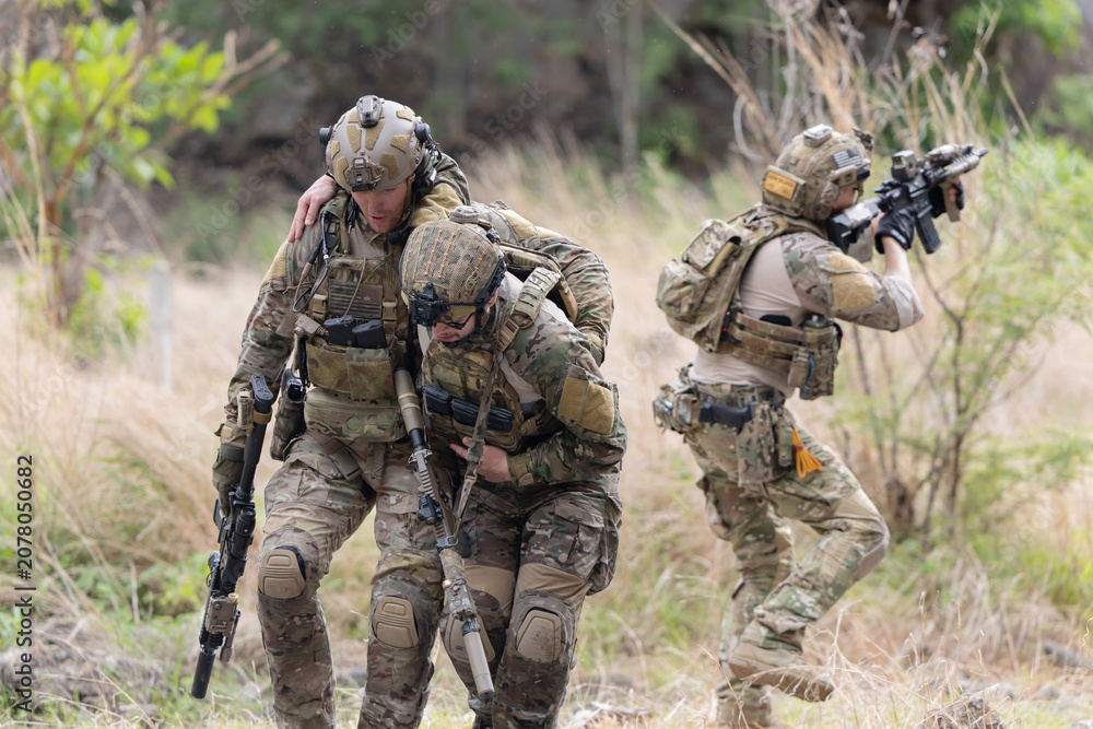 Fototapeta premium Soldier carries injured comrade over rocky terrain