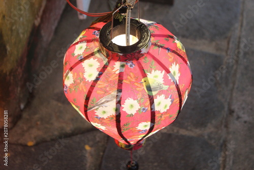 Red silk lantern with floral and bird illustration hanging at street food market.