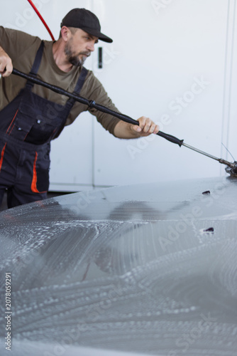 Quadro su tela Male car wash employee in workwear diligently cleaning a vehicle with a long-han