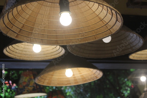 Traditional straw hat lampshades hanging from ceiling in rustic outdoor setting.