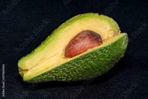 A halved Hass avocado shows its creamy yellow-green flesh and large brown pit. It rests on a dark surface, highlighting its texture. This fruit is often used in various dishes for its taste.