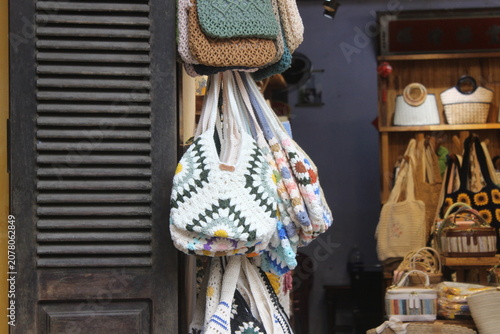 Handmade crochet tote bags with floral granny square patterns hanging inside shop.