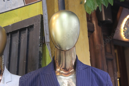 Close up portrait of golden mannequin head wearing blue pinstripe formal suit coat.