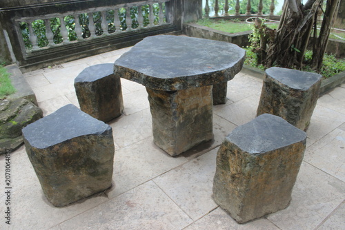 Stone table and stools set arranged on paved floor inside serene outdoor terrace.