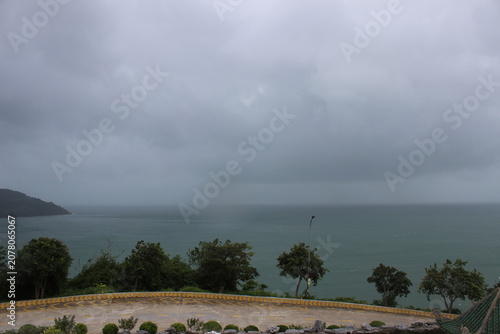 Cloudy coastal scenery viewed from elevated point above winding road with foliage.