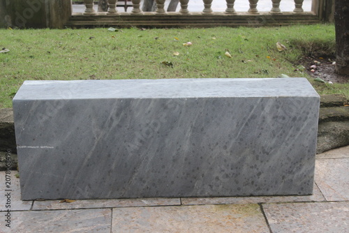 Polished grey marble bench resting on stone tiles near lush green grassy garden bed.