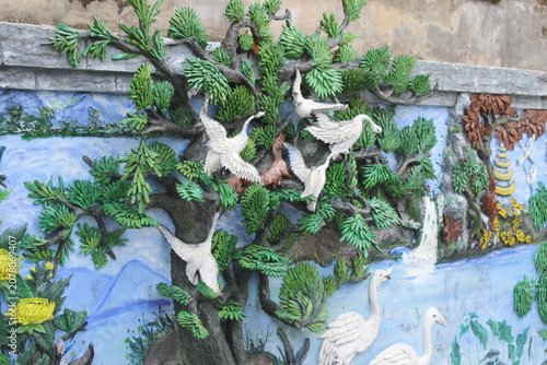 Intricate concrete wall mural showing crane birds flying above scenic landscape.