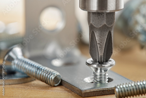 screwdriver tightens  screw into metal corner on a wooden panel. Carpentry and woodworking.