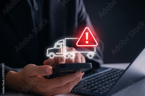 Hand Holding Smartphone with Warning Truck Symbols on Digital Screen Over Dark Keyboard Background