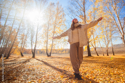 Woman walking in autumn forest with arms outstretched. Happy girl enjoying sunny fall weather in park. Seasonal lifestyle, freedom, nature connection and golden foliage scenery concept.