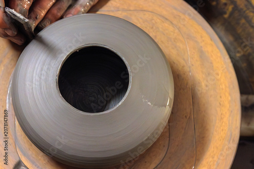Top view of a handmade clay vessel being trimmed on a pottery wheel in a ceramic studio.
