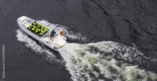 Konstfotografi RIB speedboat with passengers in safety gear cruising at high speed leaving wake
