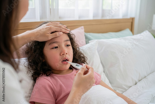 Mother checking her sick little Asian girl's temperature with digital thermometer in bed