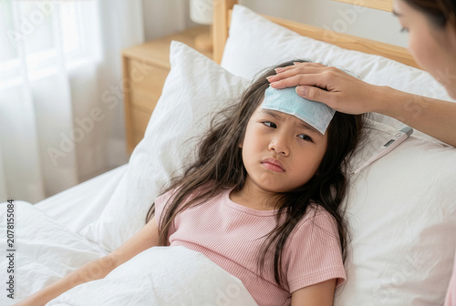Mother caring for her sick little Asian girl lying in bed with fever cooling gel patch on forehead