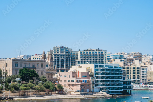 Exiles beach bay and modern buildings facing the water and towers of Balluta Parish Church, Sliema MALTA