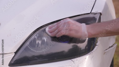 A man applies a ceramic anti-rain coating to the windows and headlights of a car.