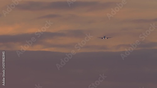 Passenger airplane flying directly towards camera through dramatic clouds during colorful sunset, telephoto close-up shot