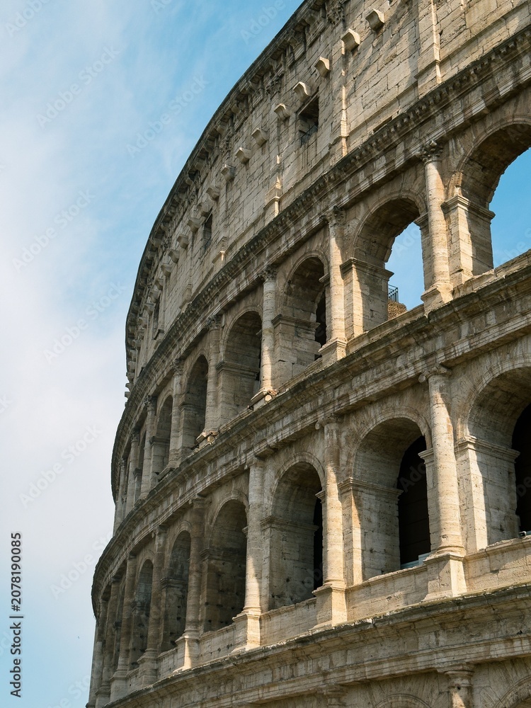 Obraz premium Ancient Roman Colosseum exterior with arched facade and stone columns against blue sky in Rome Italy