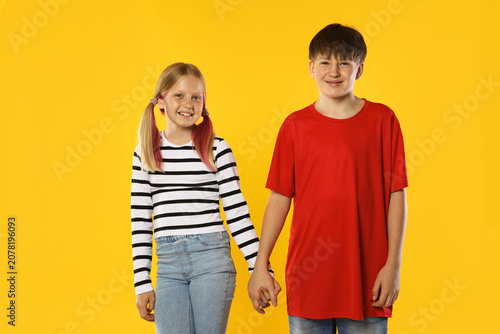 Brother and sister holding hands together on orange background
