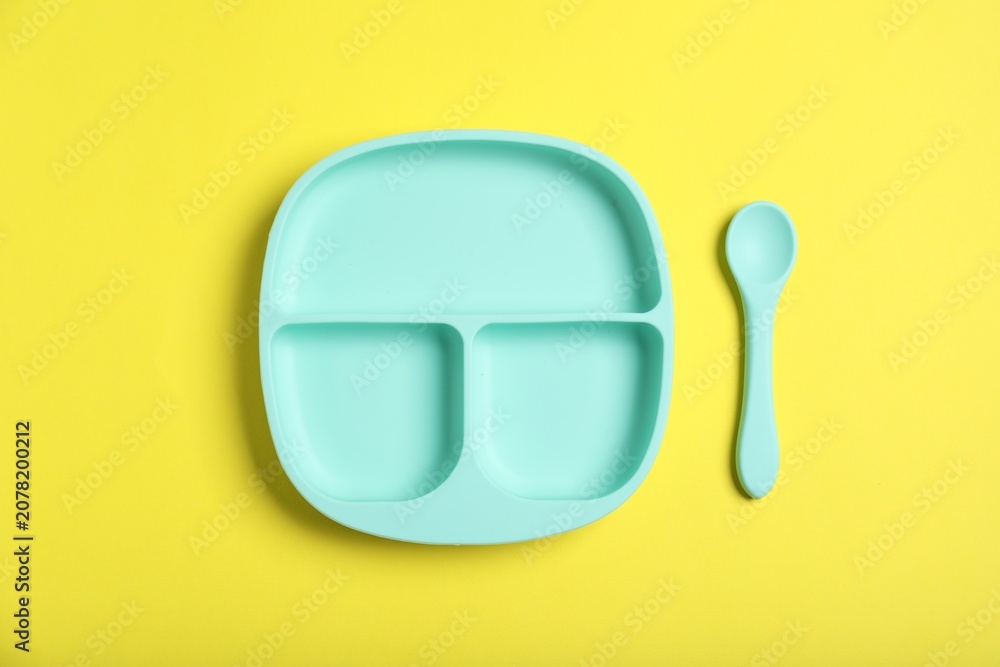 Obraz premium Plastic section plate and spoon on yellow background, flat lay