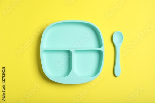 Plastic section plate and spoon on yellow background, flat lay