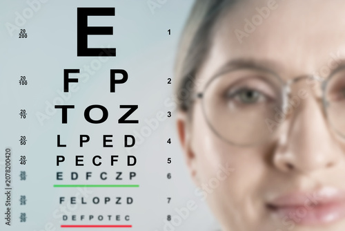 Konstfotografi Woman in glasses and eye chart on color background, selective focus