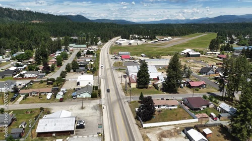 Aerial of small town and airstrip in Priest River along main street in summer with forested neighborhoods