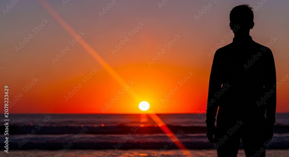 Fototapeta premium Man's silhouette against vibrant sunset ocean waves, sun rays creating dramatic light, symbolizing wellness and inspiration