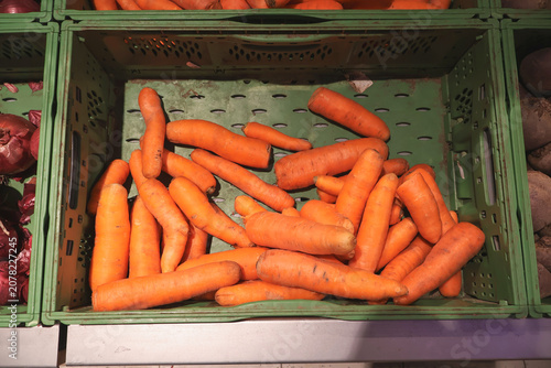 Fresh orange carrots displayed in a green plastic crate at a grocery store produce section. Healthy root vegetables arranged for sale